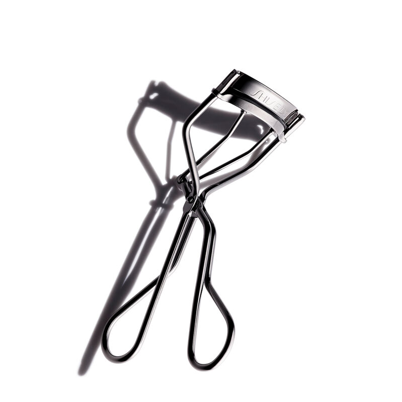 El reconocido Eyelash Curler de Shiseido, con el logotipo de Shiseido, riza y da forma a las pestañas. La herramienta de maquillaje tiene una forma curva con dos mangos que se unen con una bisagra en el medio".