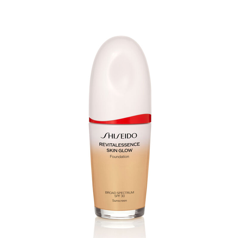"An oval-shaped bottle of Shiseido Revitalessence Skin Glow Foundation SPF 30 in shade 340 Oak. The label on the bottle is white with a red accent. The text on the label reads the product&rsquo;s title, and its sunscreen protection. "