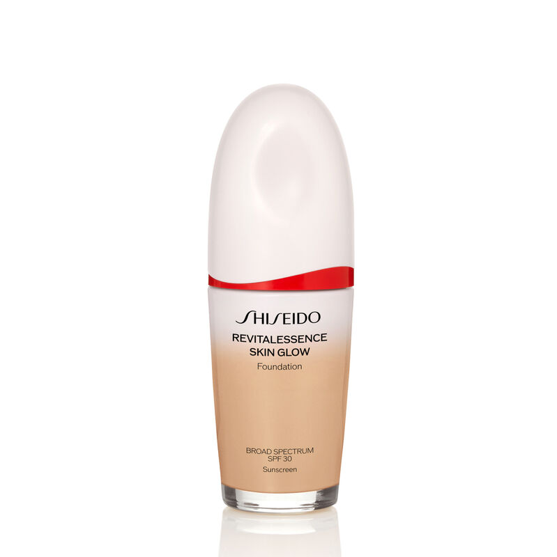 "An oval-shaped bottle of Shiseido Revitalessence Skin Glow Foundation SPF 30 in shade 310 Silk. The label on the bottle is white with a red accent. The text on the label reads the product&rsquo;s title, and its sunscreen protection. "