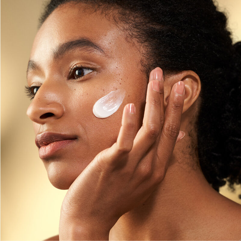 Una modelo aplicándose la crema Shiseido Vital Perfection Uplifting and Firming Advanced Cream en la parte superior del pómulo izquierdo.