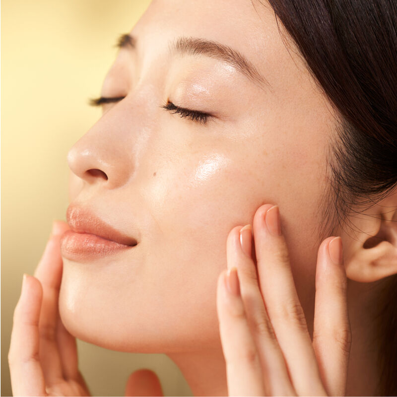 Una modelo aplicándose la crema Shiseido Vital Perfection Uplifting and Firming Advanced Cream en la parte superior del pómulo izquierdo.